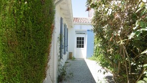 A narrow gravel path leading to a white building with blue shutters and a door. - Le relais de la Sicarde (Saint-Denis-d´Oléron)