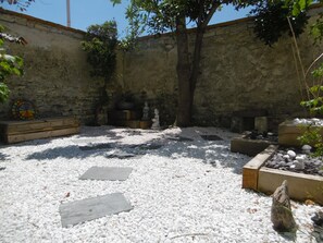 A courtyard with stone walls, a tree, and a Buddha statue.