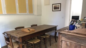 A dining area with a wooden table and chairs, a blue mug with utensils, and a framed picture on the wall. - Le relais de la Sicarde (Saint-Denis-d´Oléron)