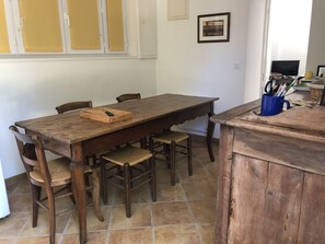 Un coin repas avec une table et des chaises en bois, une tasse bleue contenant des couverts et un tableau encadré accroché au mur.