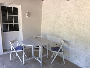 Un petit espace patio avec une table blanche et deux chaises, une porte blanche et un mur à texture.