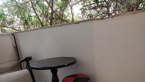 A small outdoor seating area with a round table and two chairs, one blue and one red, against a white wall with a tree visible in the background. - Cozy 2 Bedroom Apartment by The Beach (Tel Aviv)