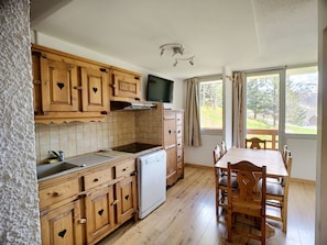 Een keuken met houten kastjes, een inbouwoven, een koelkast en een eettafel met stoelen.