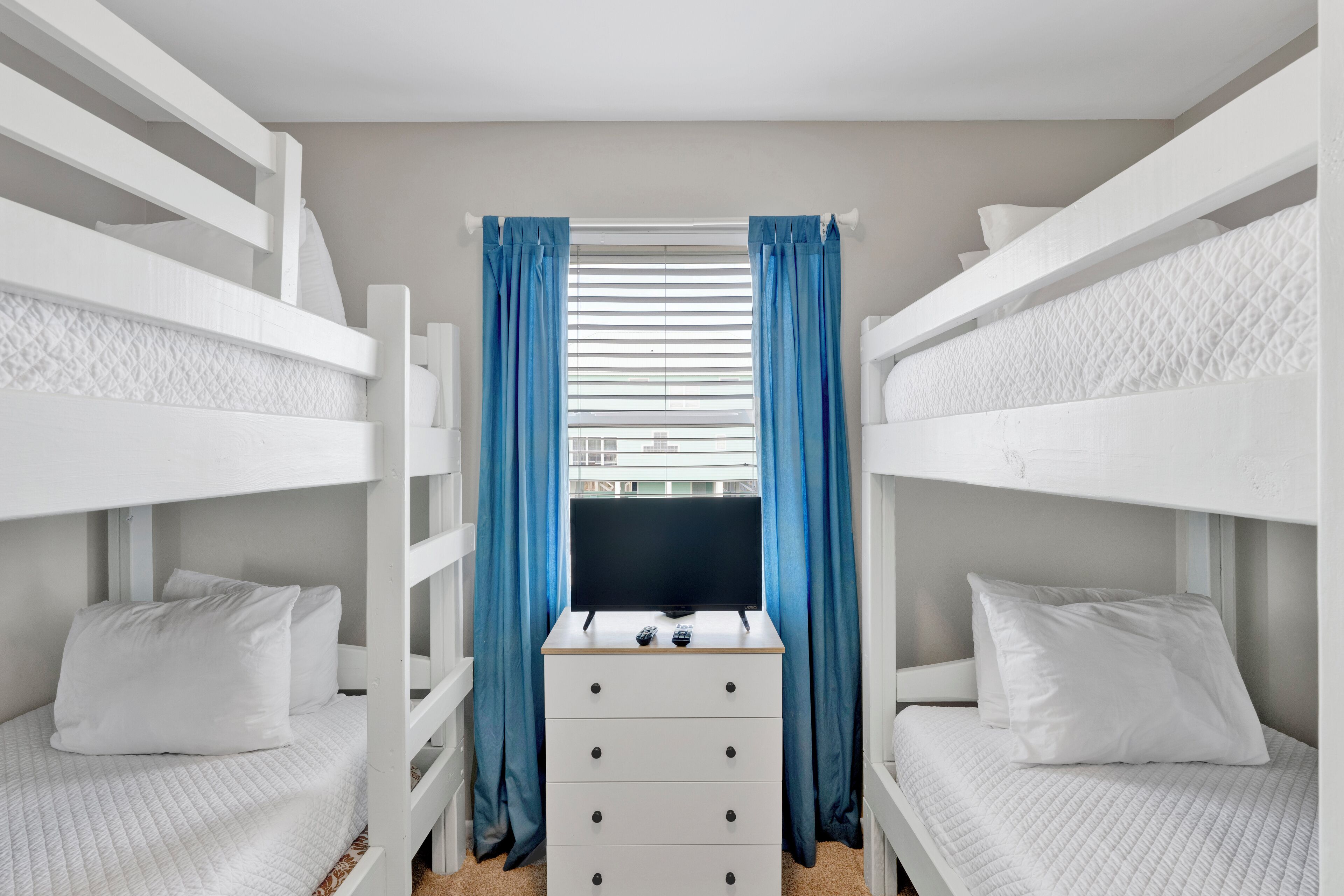 A bunk bed room with a TV on the lower bunk, a dresser, and blue curtains.