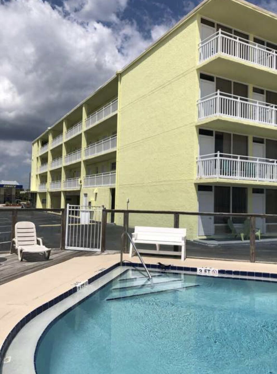 Un hôtel à plusieurs étages doté d’un espace piscine comprenant une piscine, des chaises longues et un banc blanc.