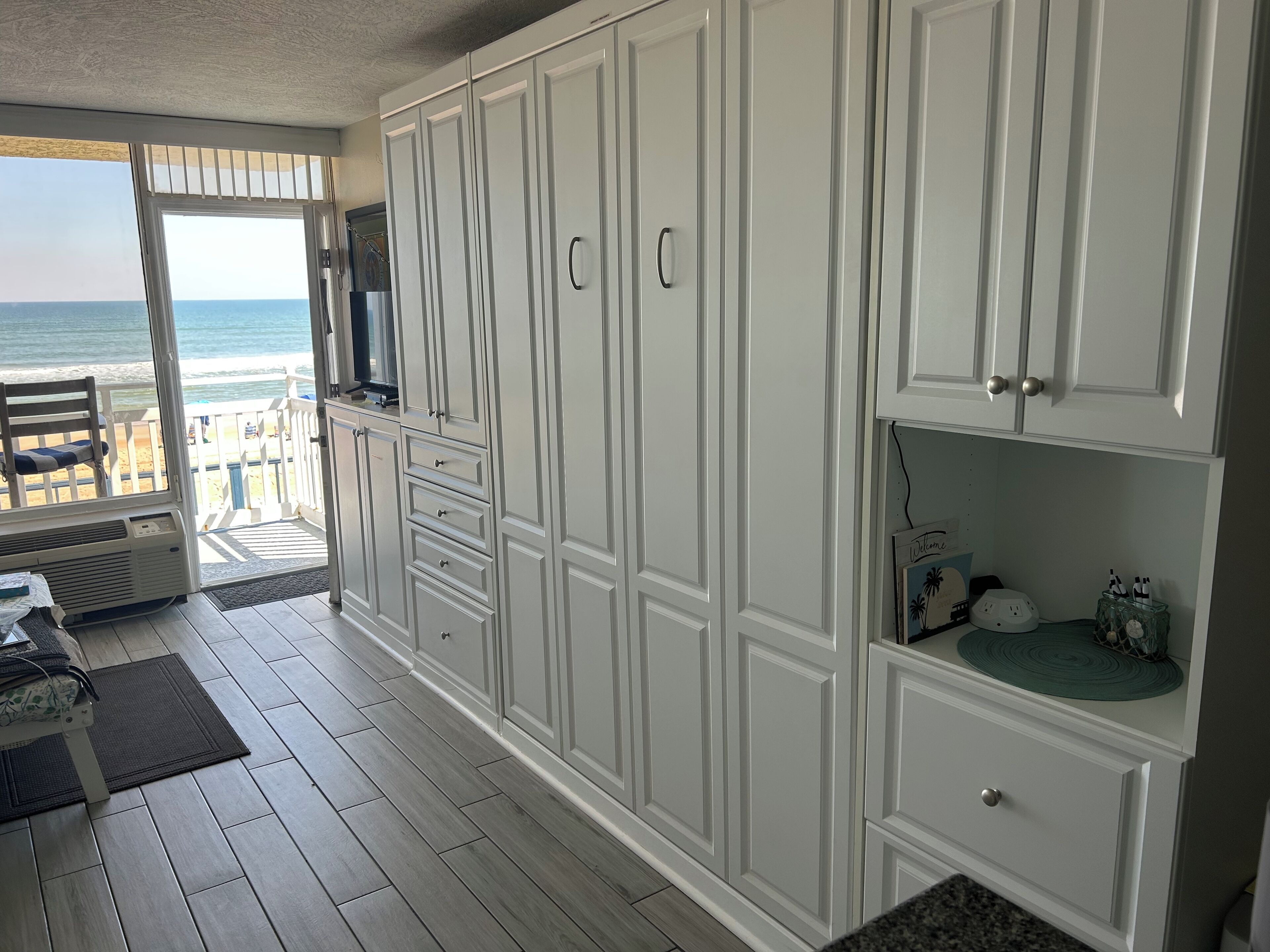 A spacious kitchen with white cabinetry, a built-in oven, and a view of the beach through a sliding glass door.