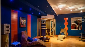 Ein moderner Spa-Bereich mit zwei Korbstühlen, einem Massagetisch und einer Holzkabine.