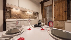 Comedor con pared de piedra, vigas de madera y muebles de cocina blancos.