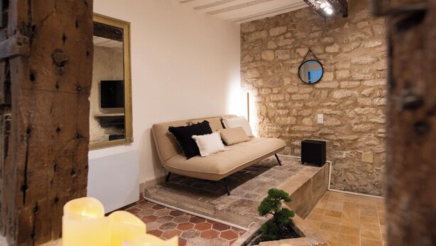 Una habitación acogedora con pared de piedra, techo de madera, un sofá y varias velas.