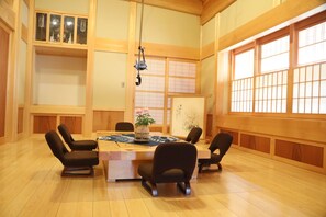 Une pièce de style japonais traditionnel, avec un sol recouvert de tatamis, une table basse et des chaises noires, ainsi qu’une grande fenêtre à panneaux coulissants de type shoji.