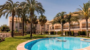 A pool surrounded by palm trees and a multi-story building with balconies.