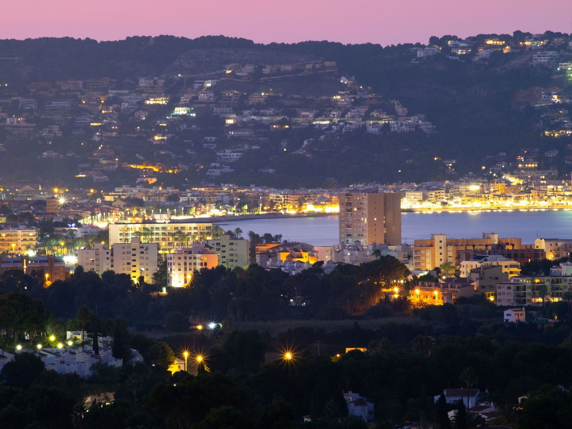 Eine Küstenstadt im Abendlicht mit beleuchteten Gebäuden und Blick auf das Meer.