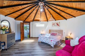 A bedroom with a sloped wooden ceiling, a bed with a canopy, a dresser, and a nightstand with a lamp.
