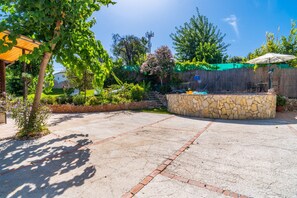 A patio with a stone wall, outdoor furniture, and a view of a garden and trees.