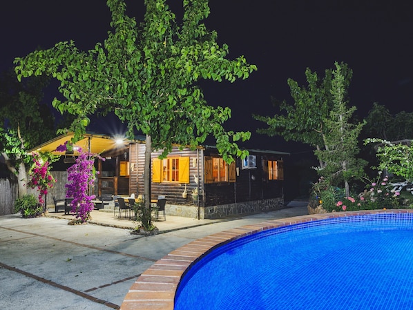 Una cabaña de madera con piscina, rodeada de árboles y plantas.