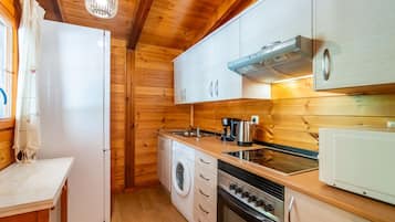 A compact kitchen with wooden walls, a built-in oven, a microwave, a sink, and a washing machine.