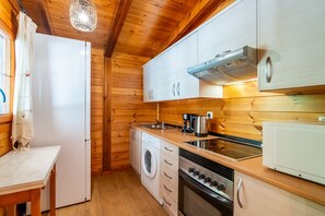 A compact kitchen with wooden walls, a built-in oven, a microwave, a sink, and a washing machine.
