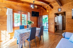 A wooden cabin with a dining table, chairs, a TV, and a bed.
