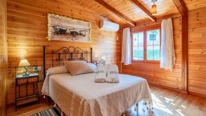 Une pièce chaleureuse, avec des murs en bois, comprenant un lit, une table de chevet, une lampe et une fenêtre avec des rideaux.