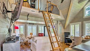 A spacious loft-style room with a wooden staircase, a dining area, and a seating area with a white sofa and red chair. - Camden Home on Lake Wateree w/ Boat Dock! (Camden)