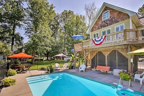 A backyard with a swimming pool, patio furniture, and a house with a balcony.