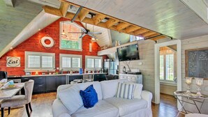 A cozy living room with a white sofa, a dining table, and a kitchen area with wooden beams and a red accent wall. - Camden Home on Lake Wateree w/ Boat Dock! (Camden)