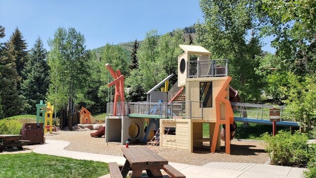 A playground with various play structures, including a slide and climbing areas, surrounded by trees and a picnic table. - Vail Studio Condo Private Balcony, Loft, HSB312 (Vail)