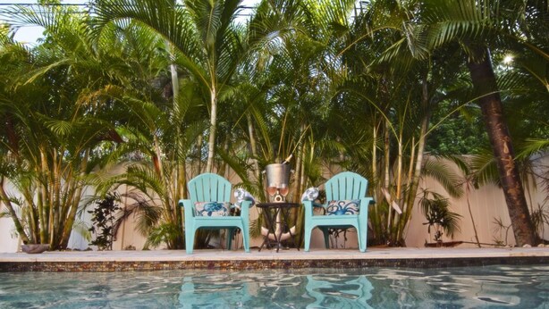 A swimming pool with two turquoise chairs and a small table, surrounded by palm trees. - Dix-Sea-Land Delight: Close to beach, private pool, quiet street (Bradenton Beach)