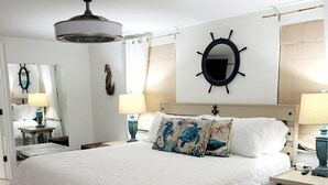 A neatly arranged bedroom with a large bed, a ceiling fan, a ship's wheel decoration, and two bedside lamps. - Dix-Sea-Land Delight: Close to beach, private pool, quiet street (Bradenton Beach)