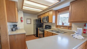 A compact kitchen with wooden cabinets, a stainless steel microwave, a black refrigerator, a gas stove, and a sink. - Edgewater #10 , Magnificent Panoramic view of June Lake through lg picture window (June Lake)