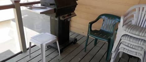 A balcony with a grill, a small white table, and two plastic chairs.