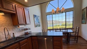 A kitchen with wooden cabinets, a stainless steel dishwasher, and a large window offering a view of the outdoors. - Lakefront retreat with big views | Freshly renovated (June Lake)