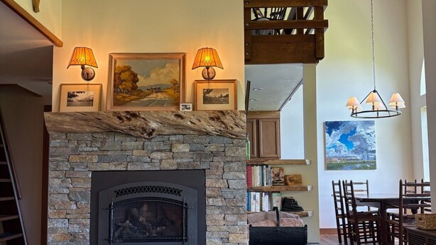 A cozy living room with a stone fireplace, wooden beams, and a dining area with wooden furniture. - Lakefront retreat with big views | Freshly renovated (June Lake)