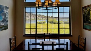 A dining area with a table and chairs, a large window with a view of a lake and hills, and a chandelier. - Lakefront retreat with big views | Freshly renovated (June Lake)