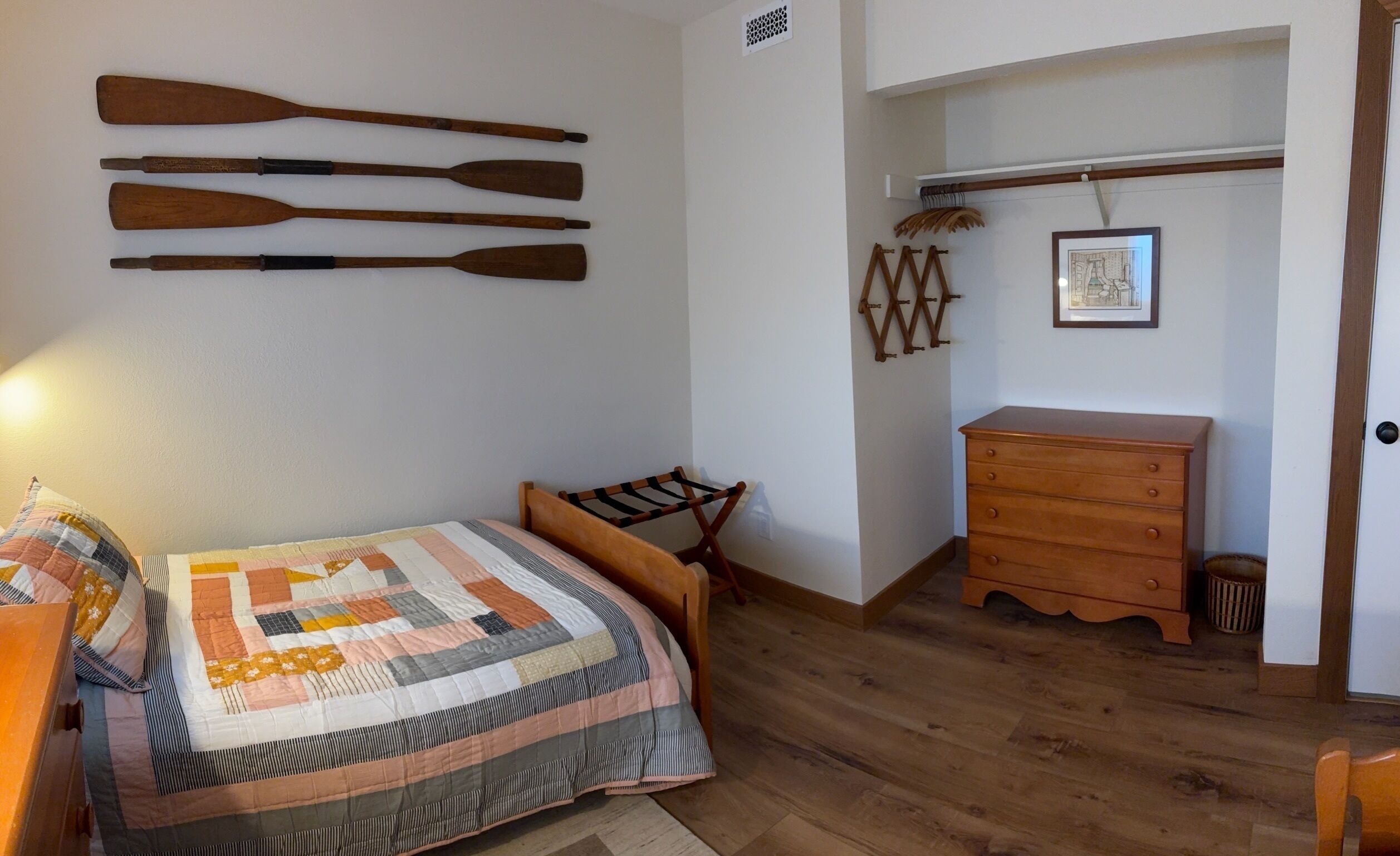 A bedroom with a wooden bed, a wooden dresser, and a wall-mounted drying rack.