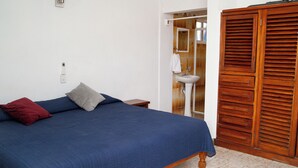 A bedroom with a bed, a wooden wardrobe, a bathroom with a sink, and a white wall with a light switch. - Casa Bahía Department 1 (Centro)
