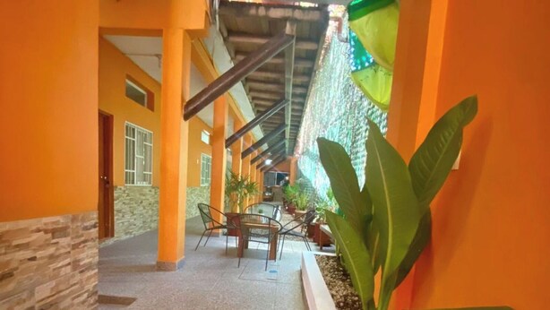 A corridor with orange walls, a stone wall on one side, and a tiled floor. There is a table with chairs and a potted plant in the center. - Casa Bahía Department 1 (Centro)