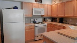 A compact kitchen with wooden cabinets, a white refrigerator, a microwave, and a stove. - Hideaway #103, views of Carson Peak (June Lake)