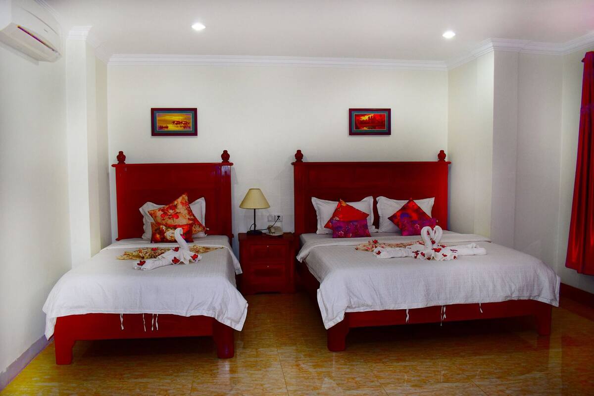A hotel room with two red beds, white bedding, and red curtains.