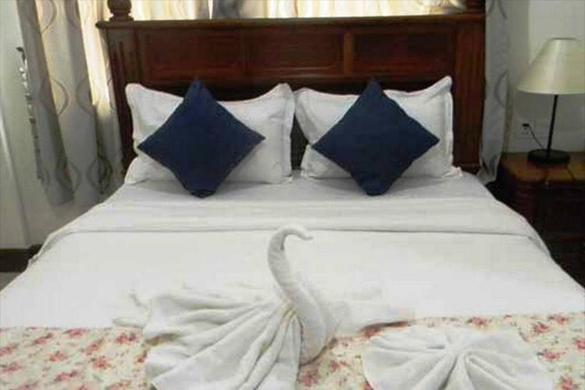 A neatly made bed with white linens and two blue pillows, a floral-patterned blanket, and a wooden headboard.
