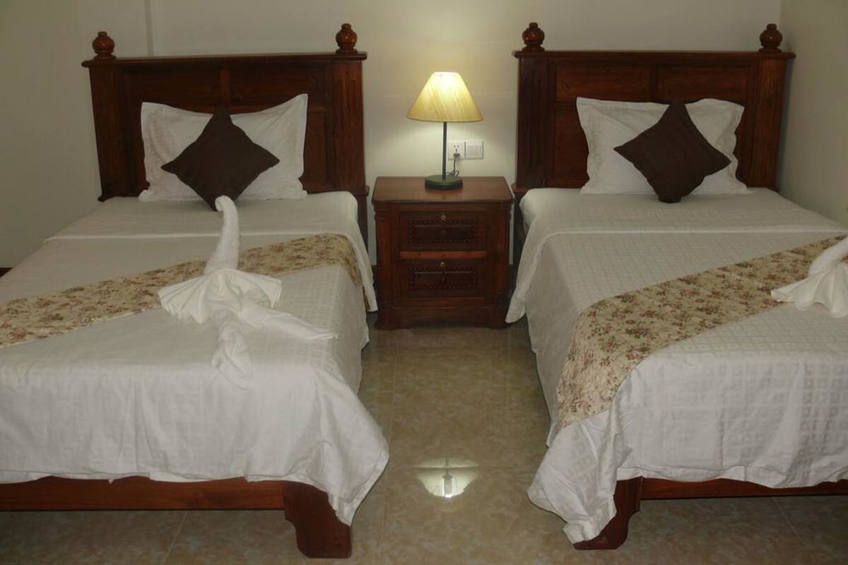Two double beds with wooden headboards, a bedside table with a lamp, and a floral bedspread.