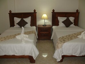 Two double beds with wooden headboards, a bedside table with a lamp, and a floral bedspread. - Vanne Hotel (Battambang)