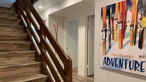 A wooden staircase with a handrail and a wall with a colorful poster that reads "True Mountain ADVENTURE". - Edgewater #4 NEWLY RENOVATED! “GARAGE PARKING“ EN-SUITE KING SIZE BED (June Lake)
