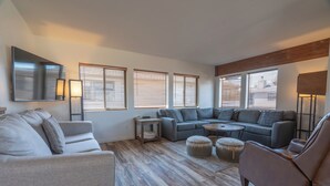 A modern living room with a sectional sofa, ottomans, a coffee table, and a TV mounted on the wall. - Edgewater #4 NEWLY RENOVATED! “GARAGE PARKING“ EN-SUITE KING SIZE BED (June Lake)