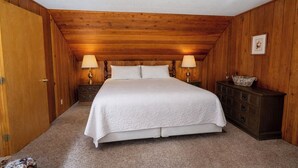 A bedroom with a wooden ceiling, a bed with white bedding, two bedside lamps, a dresser, and a framed picture on the wall. - Smith Mountain Home CUP18-009 AP 18-004 (June Lake)