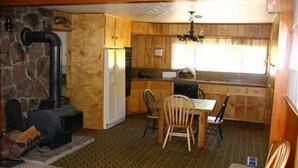 A rustic kitchen with a stone wall, wooden cabinets, a built-in stove, and a dining area with a table and chairs. - Smith Mountain Home CUP18-009 AP 18-004 (June Lake)