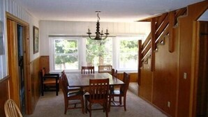 A dining room with a wooden table and chairs, a chandelier, and large windows with a view of greenery. - Smith Mountain Home CUP18-009 AP 18-004 (June Lake)