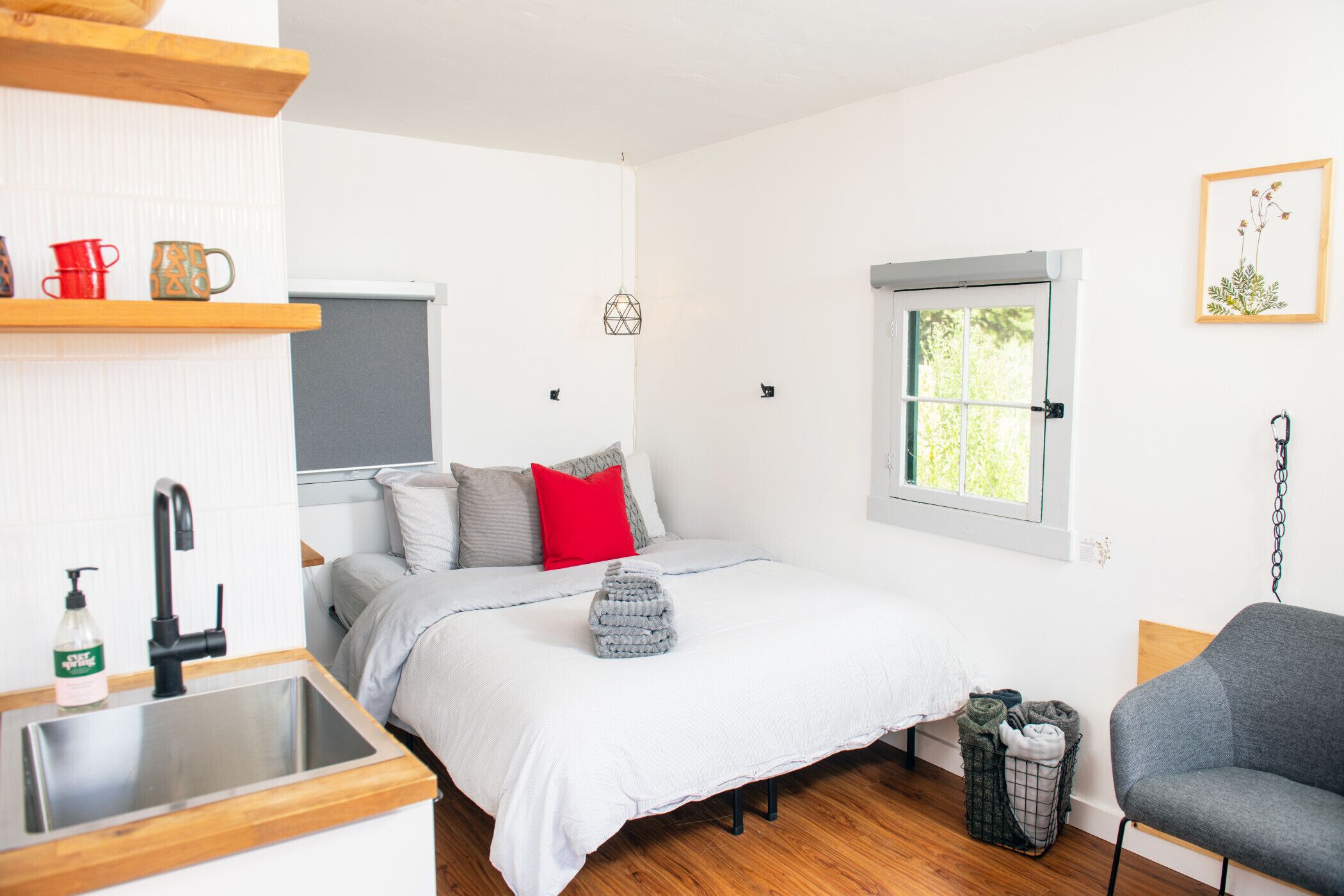 A compact bedroom with a bed, a small kitchenette, a window, and a gray chair.