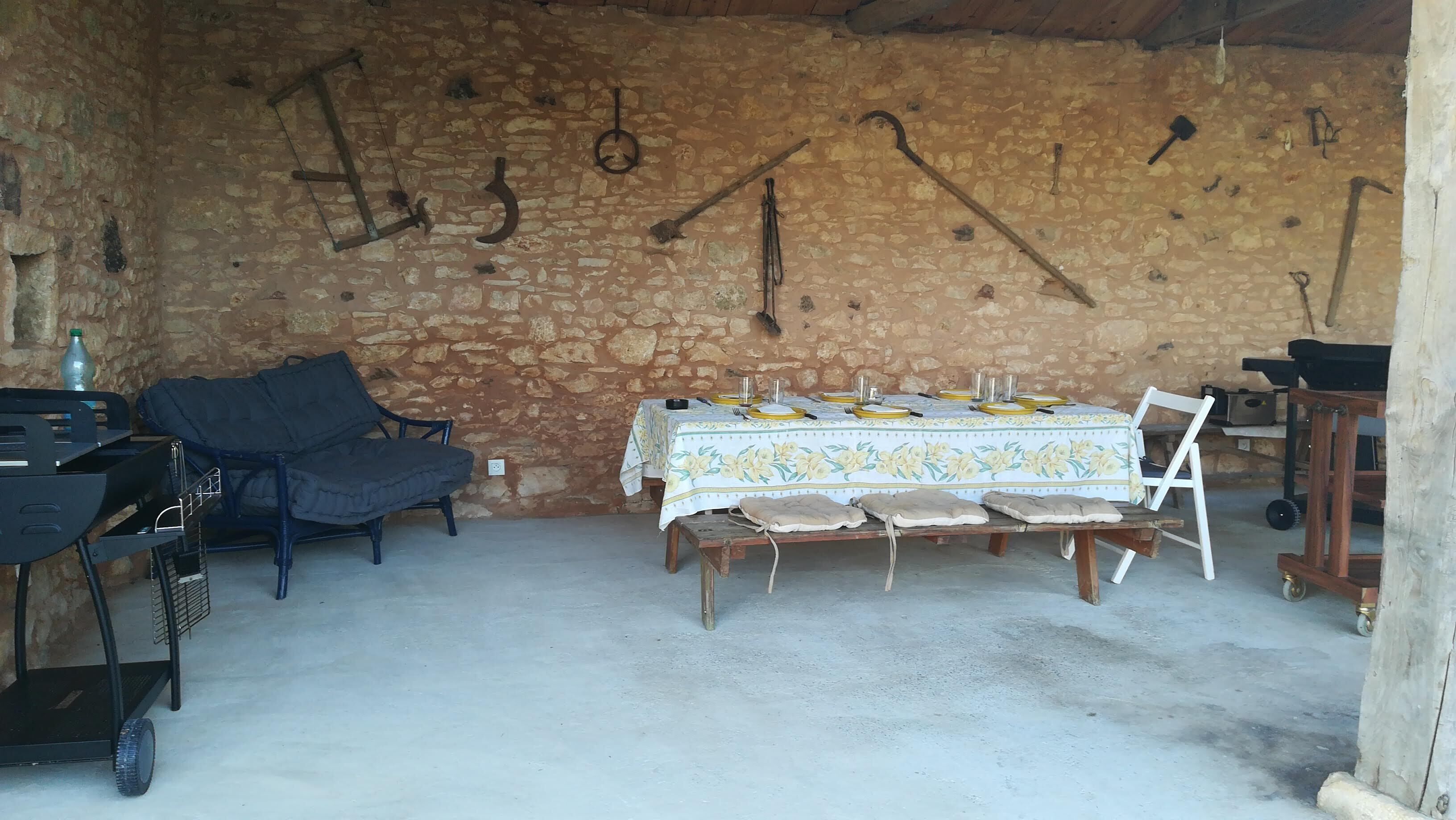 A rustic stone-walled room with a table set for four, a sofa, and a cart with a bottle.