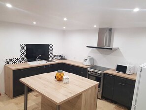 A compact kitchen with a sink, stove, microwave, and a small table with a fruit bowl. - Stone holiday house (Blanquefort-sur-Briolance)